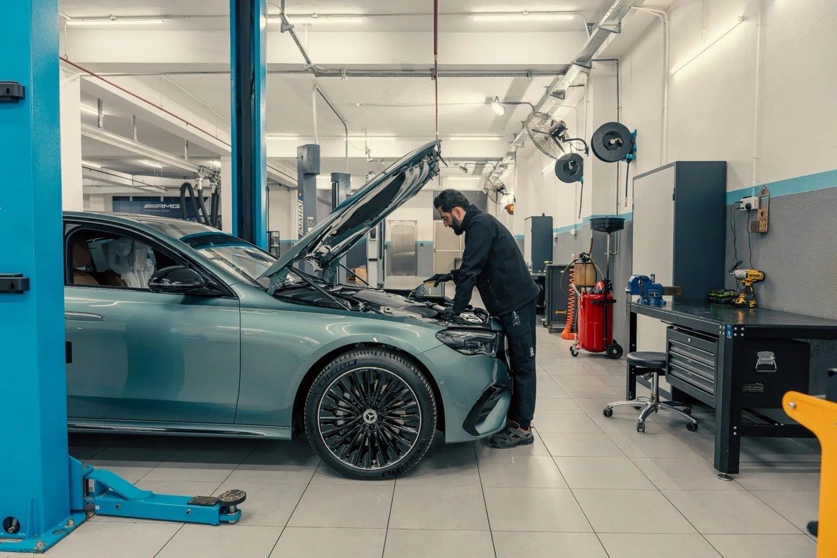 A car on a lift in a service bay with a technician at the open hood